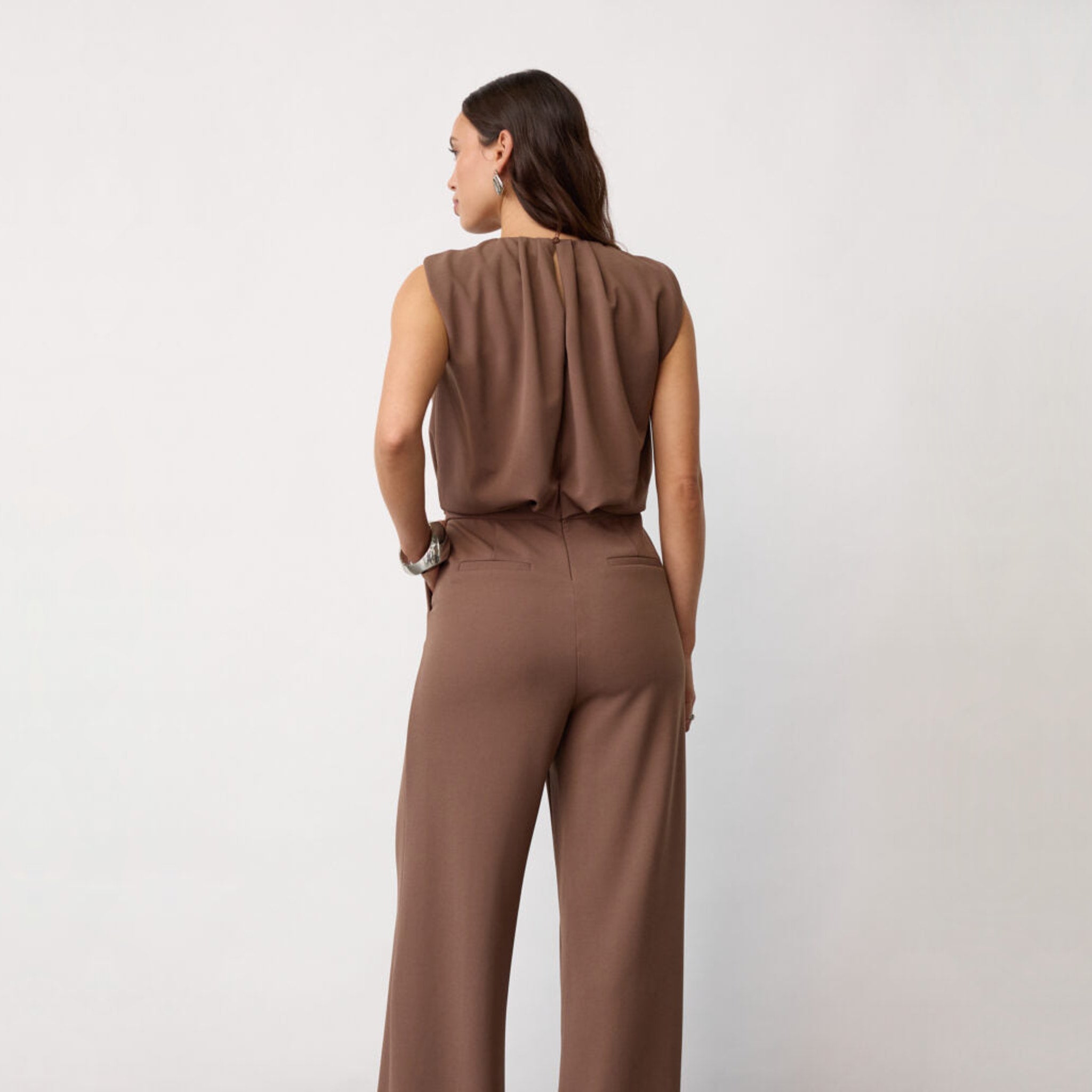 Model i brun jumpsuit set bagfra med læg i ryggen og lommer bagpå