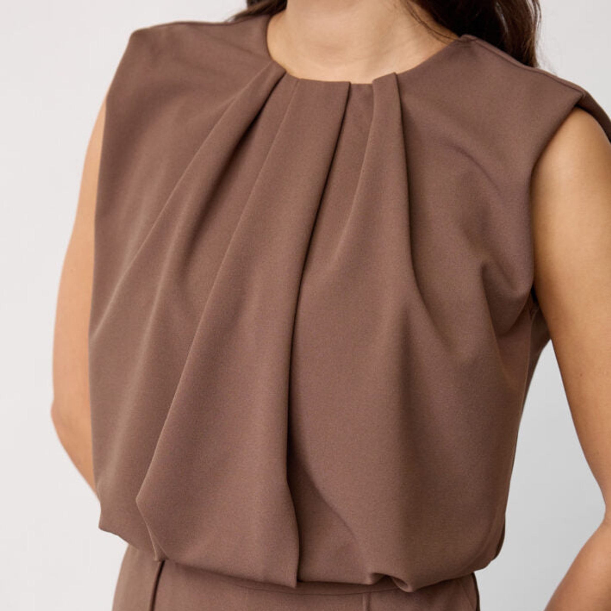 Nærbillede af læg ved halsen og draperet overdel på brun jumpsuit