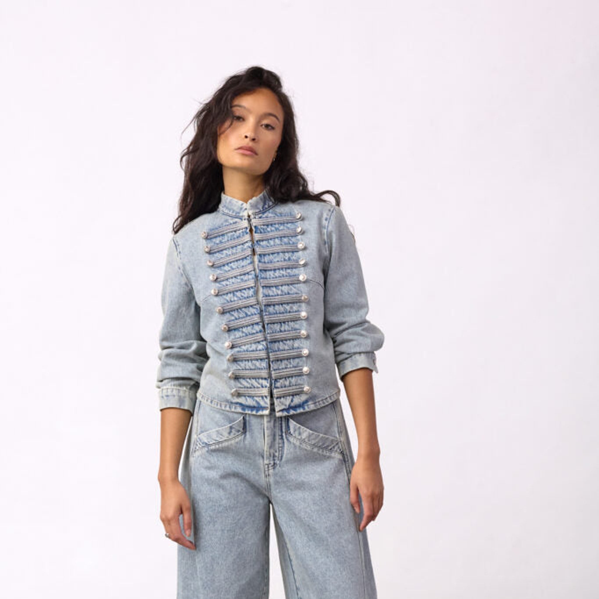 Model i blå denimjakke med standkrave og snore med sølvknapper foran, set forfra i hel figur