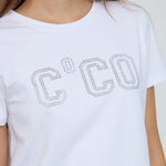 Nærbillede af C'CO-logo af små sølvfarvede sten på hvid t-shirt