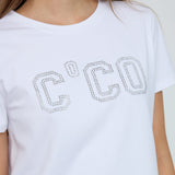 Nærbillede af C'CO-logo af små sølvfarvede sten på hvid t-shirt