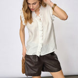 Model i hvid top med flæser ved halsudskæring og forstykke, stylet med brune shorts