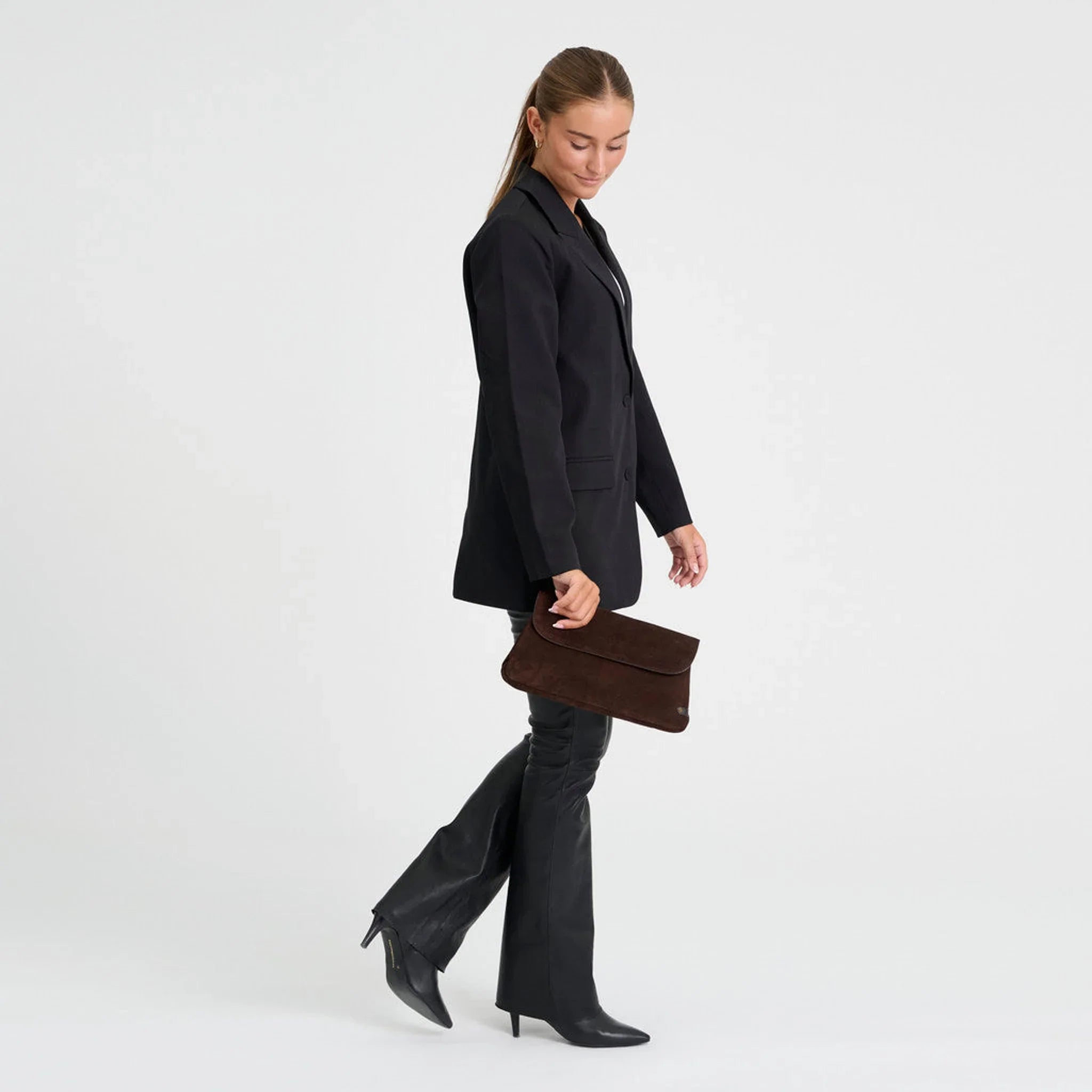 Model holder brun taske i ruskind til sort blazer og sorte bukser, set fra siden