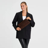 Model holder brun taske i ruskind foran sort blazer og hvid top, set forfra