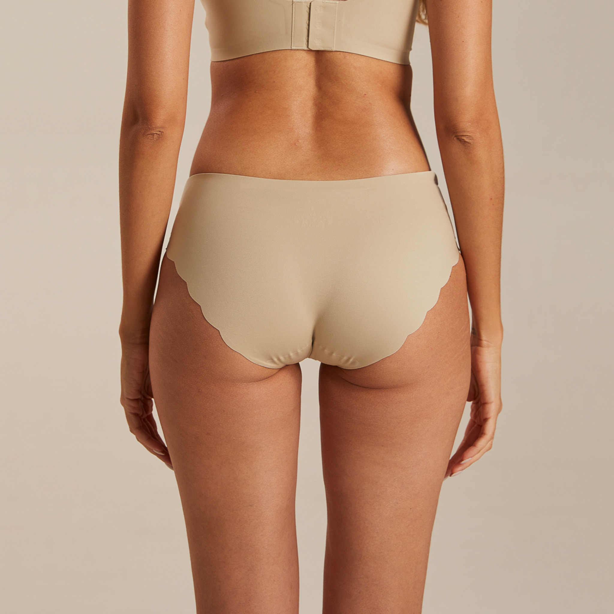 Beige Tai trusser fra Femifemme i farven Sand set bagfra med bølget kant ved benene