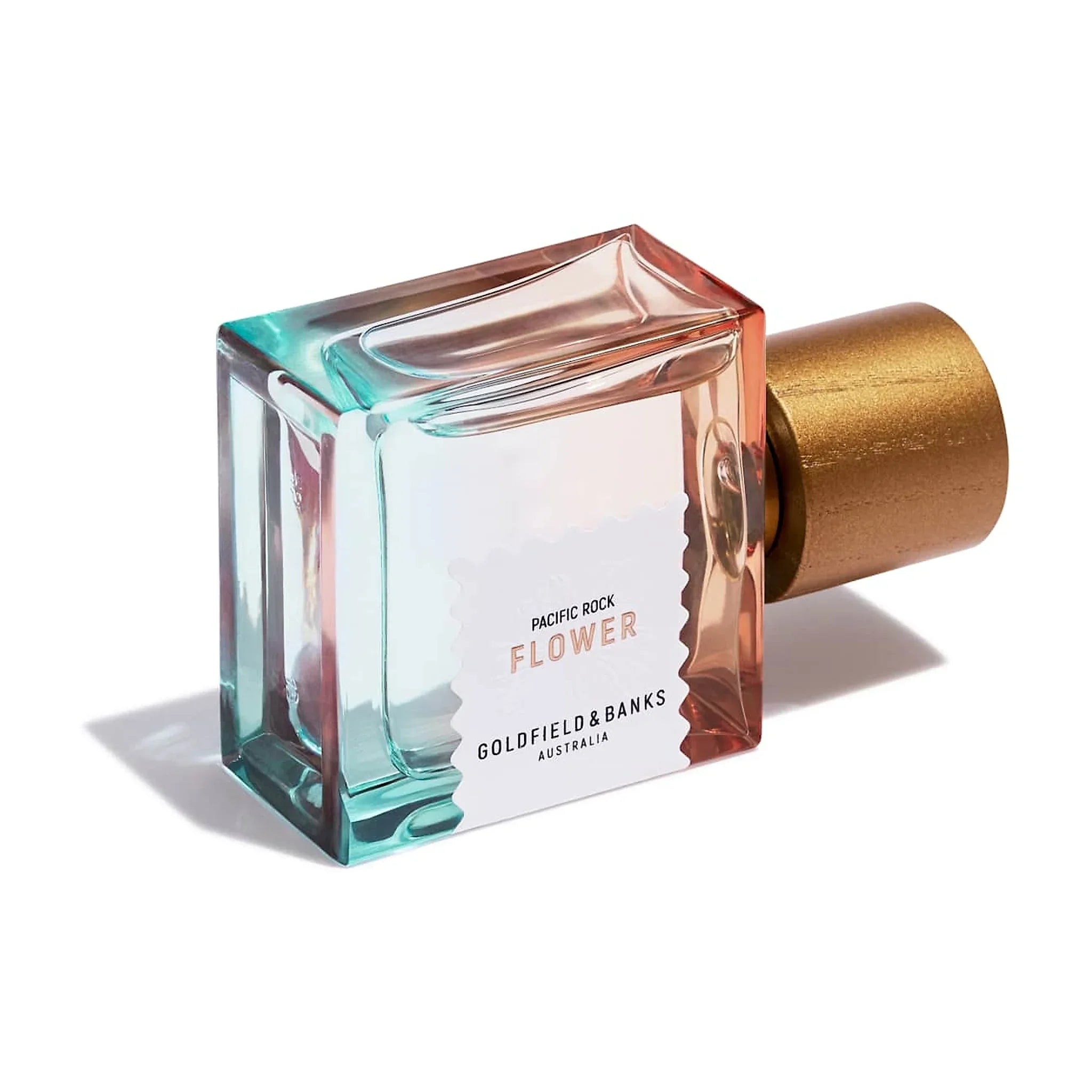 Pacific Rock Flower parfume liggende på siden, set skråt ovenfra med hvid etiket og guldfarvet låg