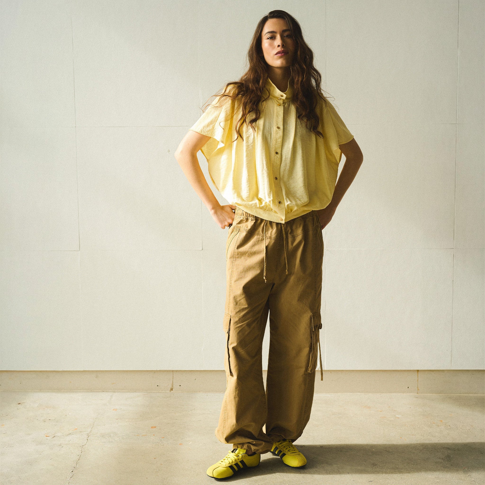 Model i brune cargobukser Mea Pant fra Gossia med vide ben, stylet med gul skjorte og gule sneakers