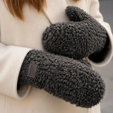 Model med mørkebrune teddy-handsker med Fashion Gloves-label ved håndleddet og cremefarvet frakke