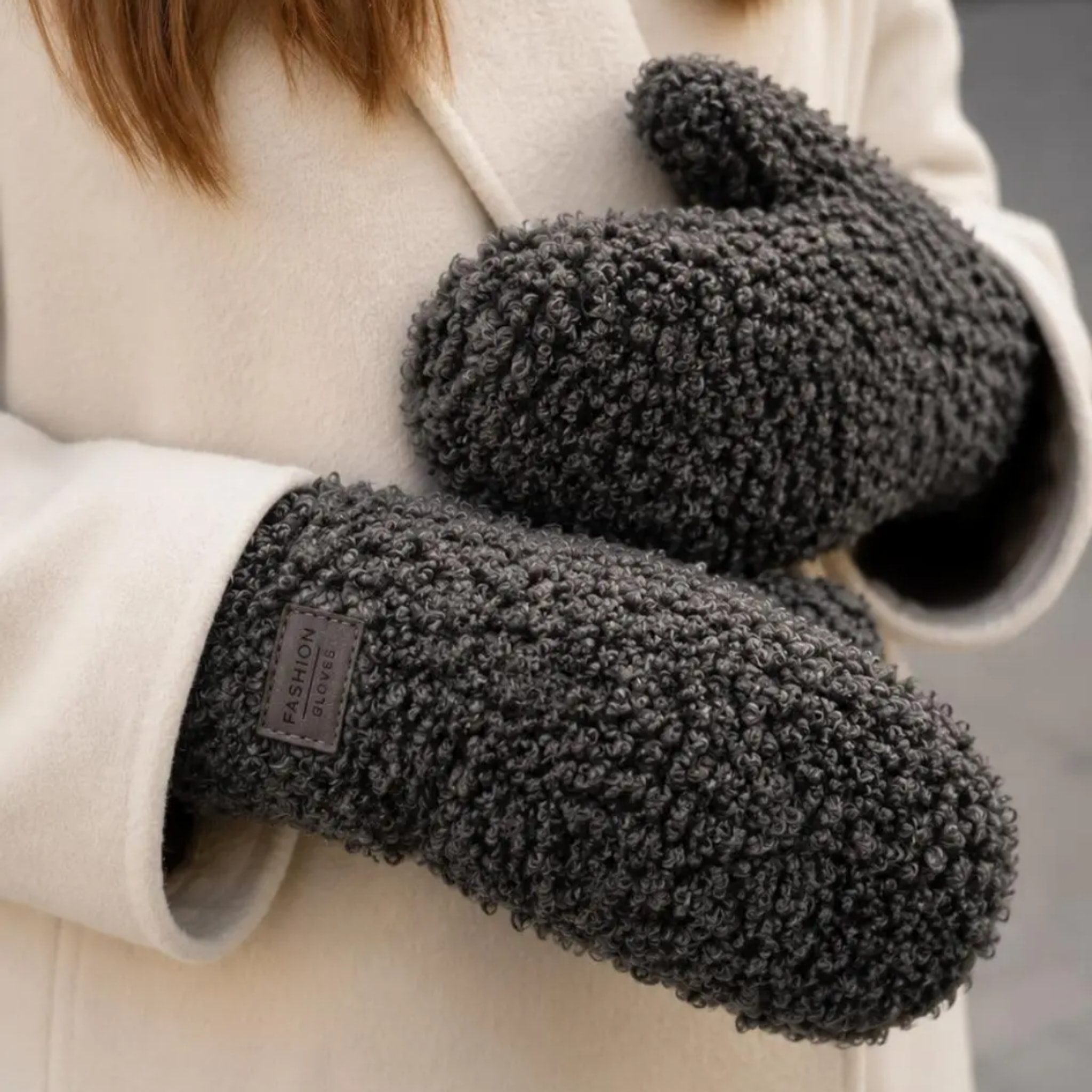 Model med mørkebrune teddy-handsker med Fashion Gloves-label ved håndleddet og cremefarvet frakke