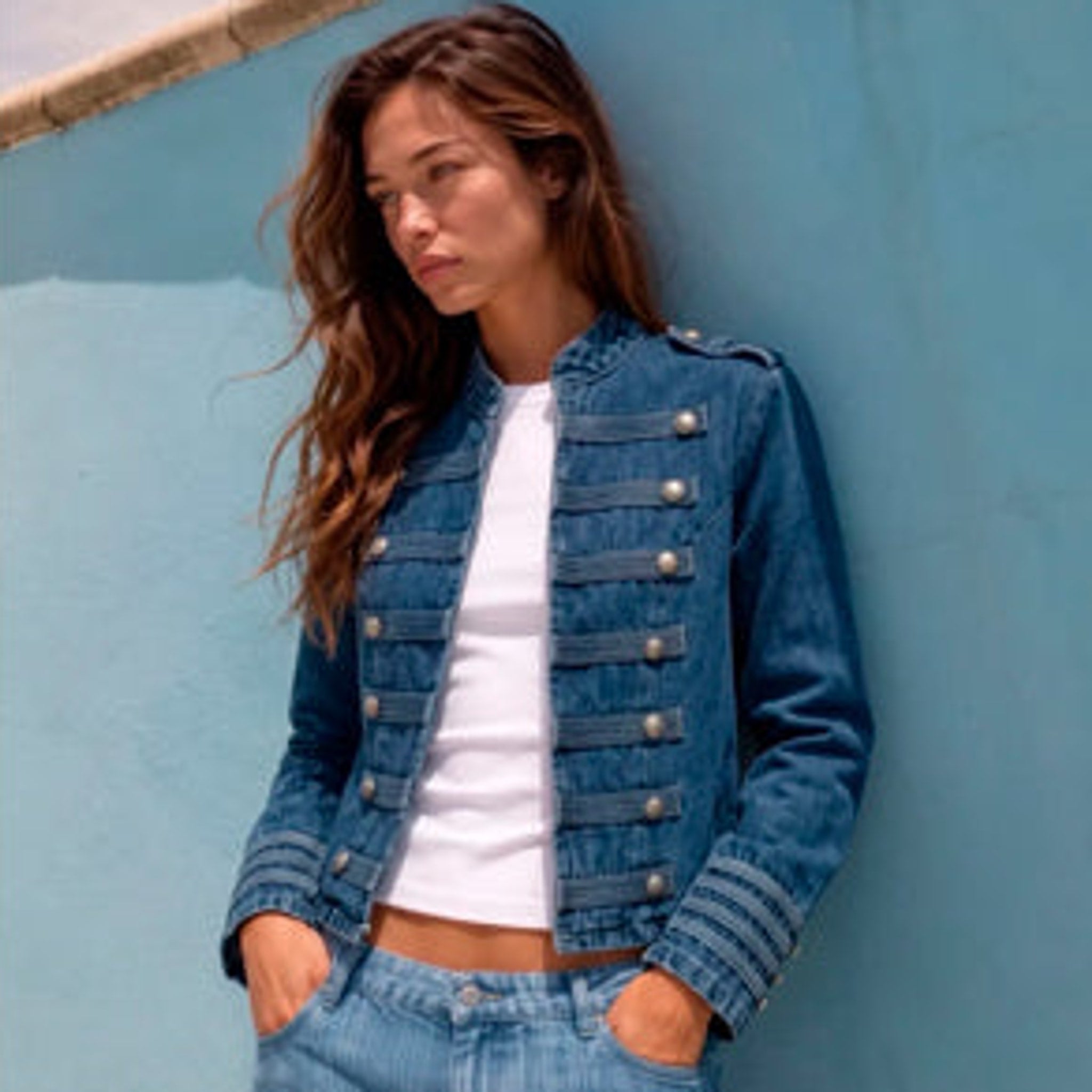 Blå denimjakke i officer-stil med standkrave, sølvfarvede knapper og snoredetaljer, stylet med hvid top og lyse jeans