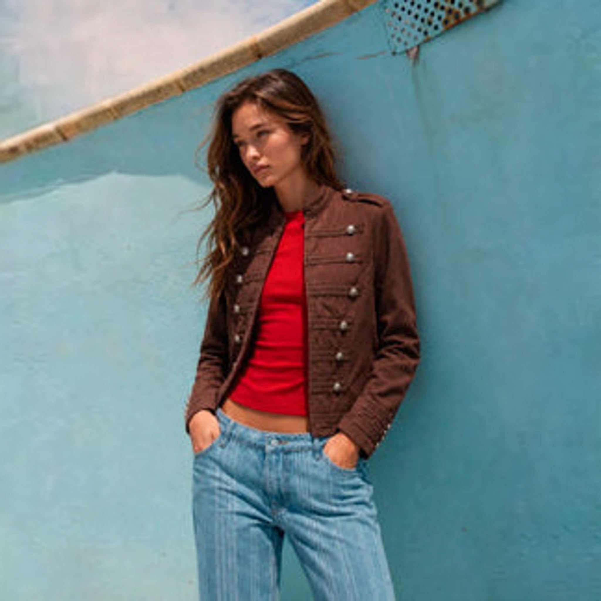 Brun denimjakke i officer-stil med standkrave og sølvfarvede knapper, stylet med rød top og lyse jeans