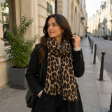 Model med brunt tørklæde med leopardprint viklet om halsen over en sort frakke og en lys strikbluse