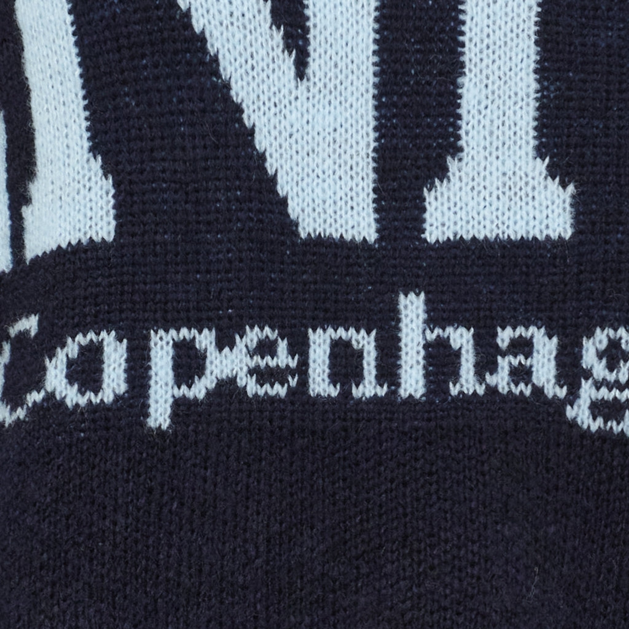 Nærbillede af strikket lyseblå Copenhagen-tekst på navy strik fra Marta du Chateau