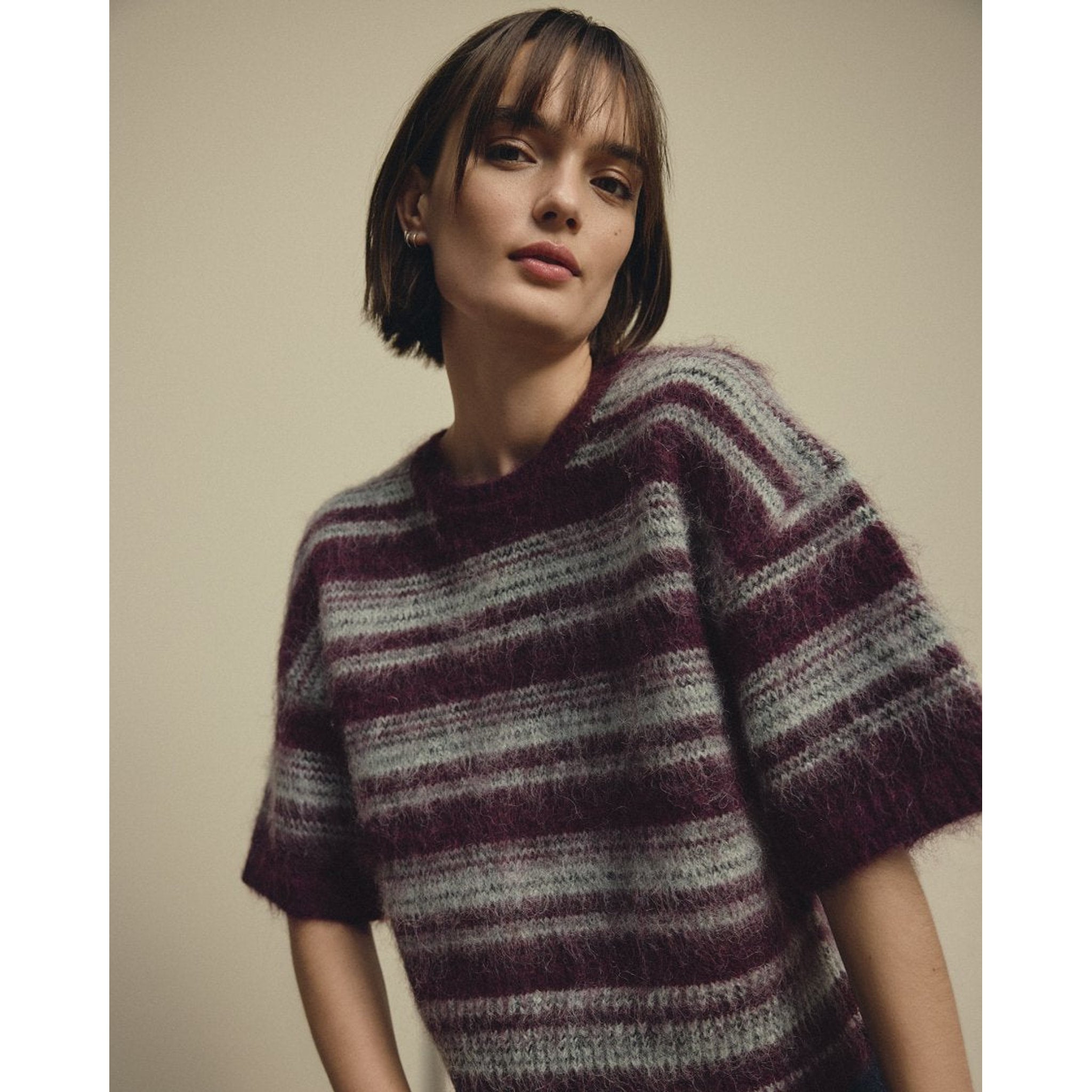 Model i kortærmet stribet pullover i lilla og grå strik med rund hals, tæt på