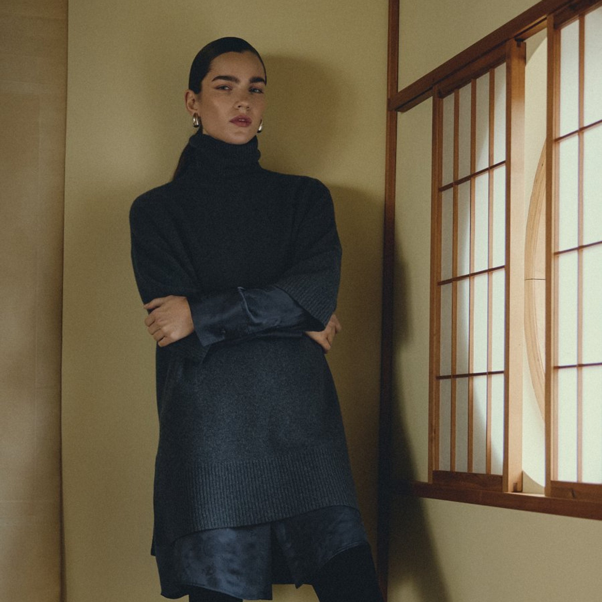 Model med krydsede arme i lang navy pullover med rullekrave stylet over satinskjorte
