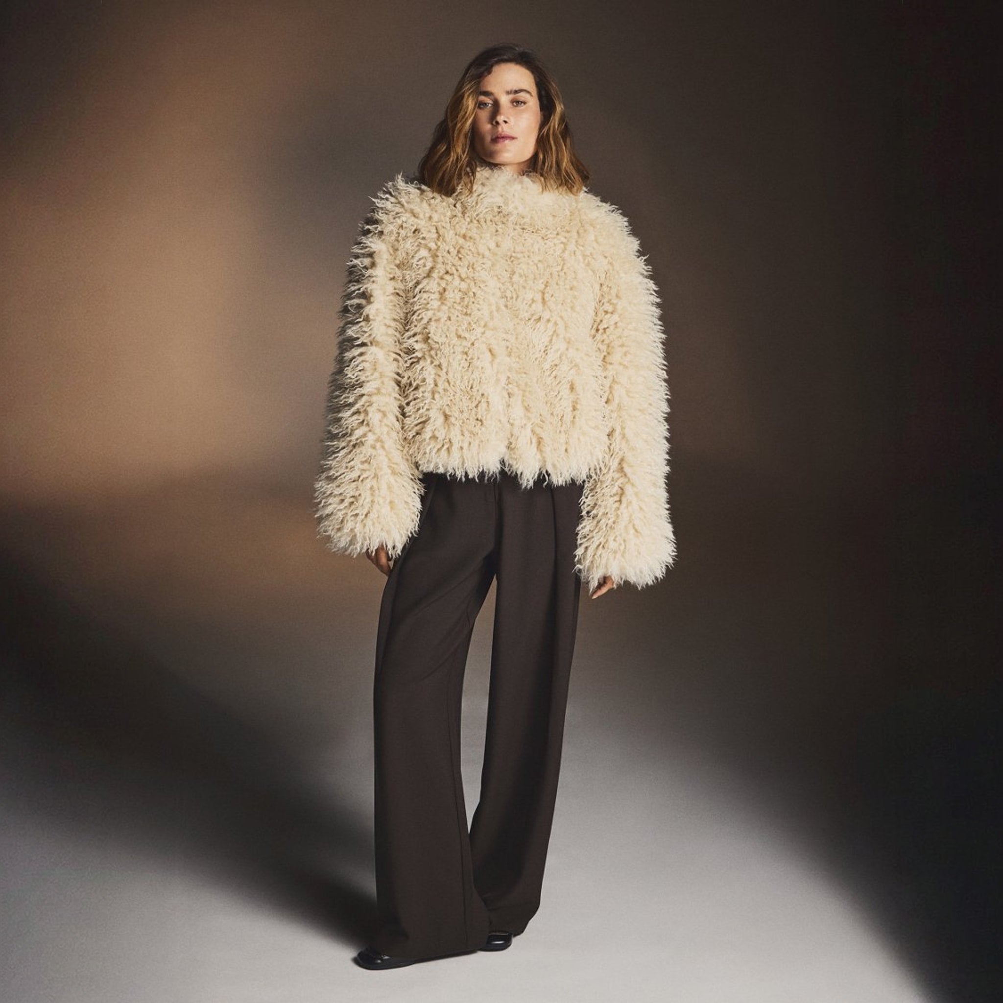Model i brune wide leg bukser stylet med en cremefarvet fluffy sweater og sorte sko