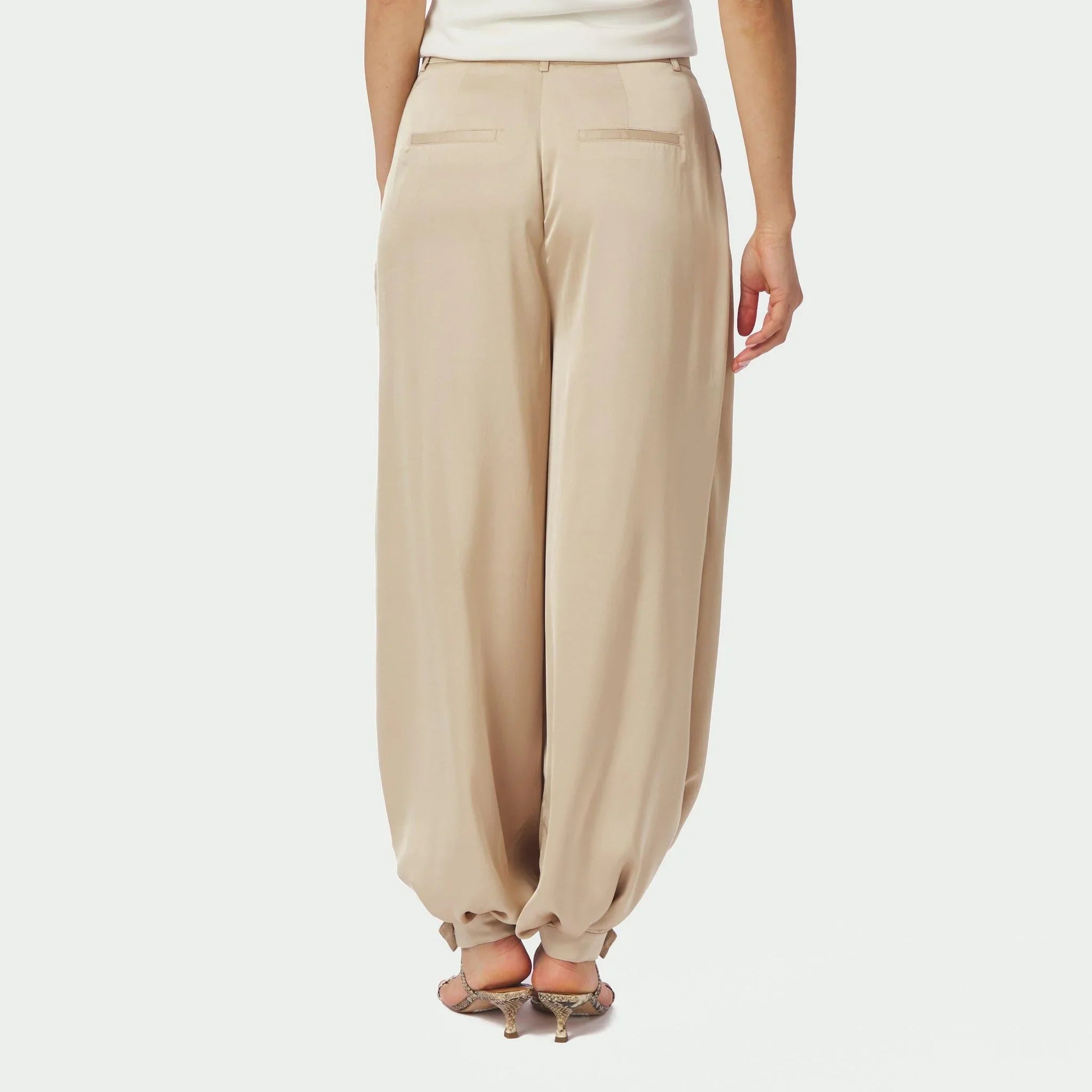 Model i beige Fayla satinbukser set bagfra med lommer og manchetter ved anklen