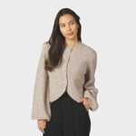 Model i beige fluffy cardigan med knapper foran og sorte bukser, set forfra