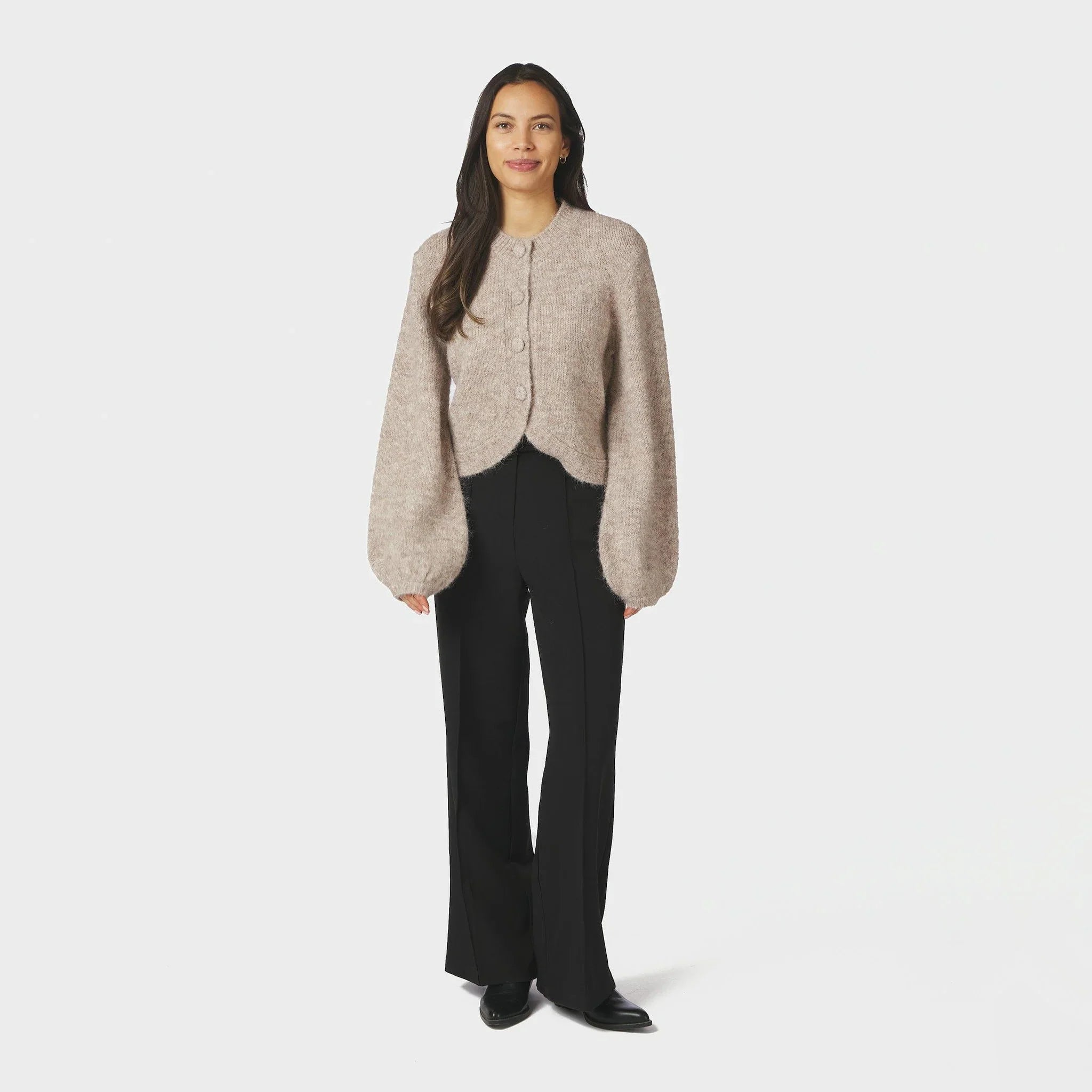 Model i hel figur med beige fluffy cardigan, sorte bukser og sorte støvler
