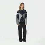 Model i oversize navy strik med argyle mønster og sorte bukser, hele figuren forfra