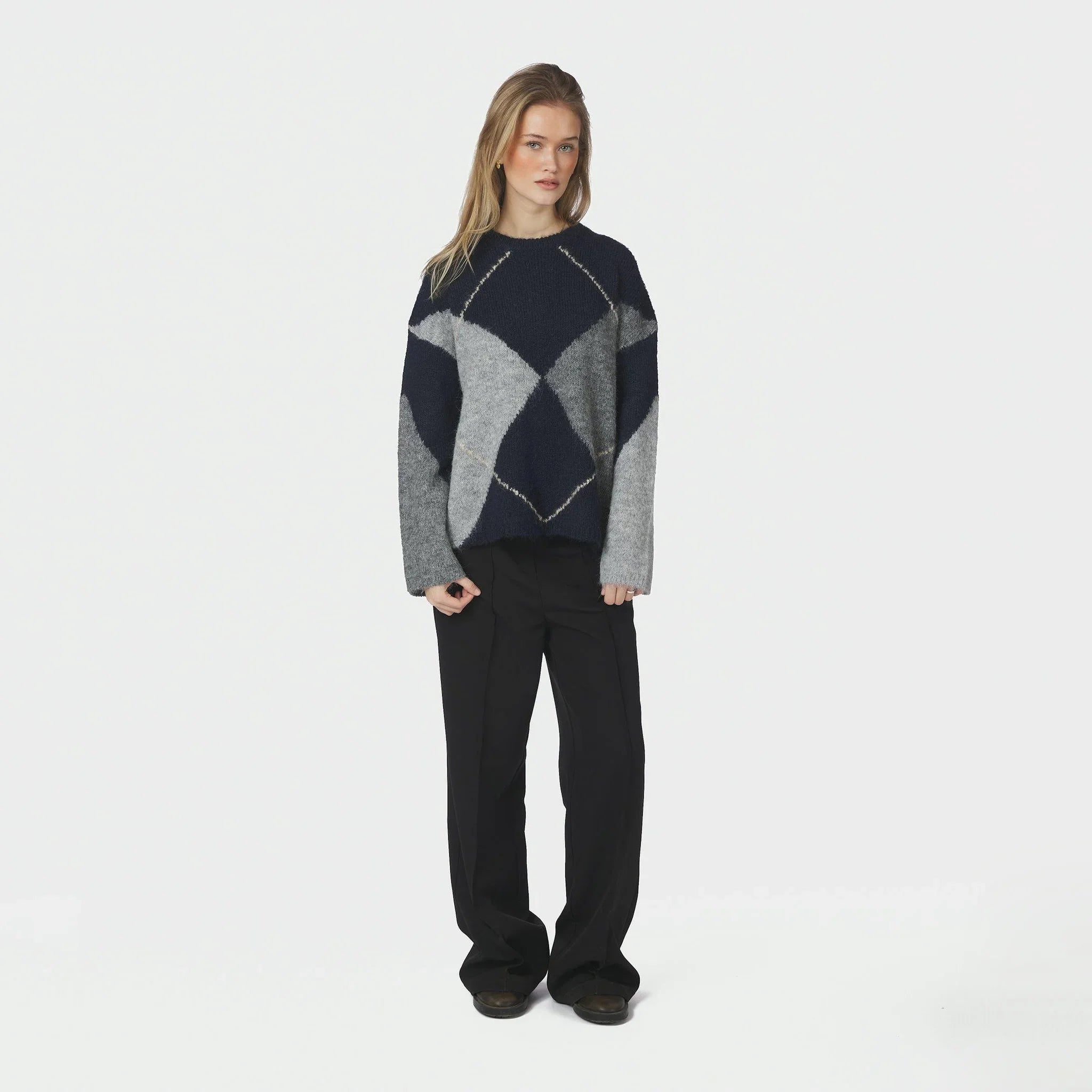 Model i oversize navy strik med argyle mønster og sorte bukser, hele figuren forfra