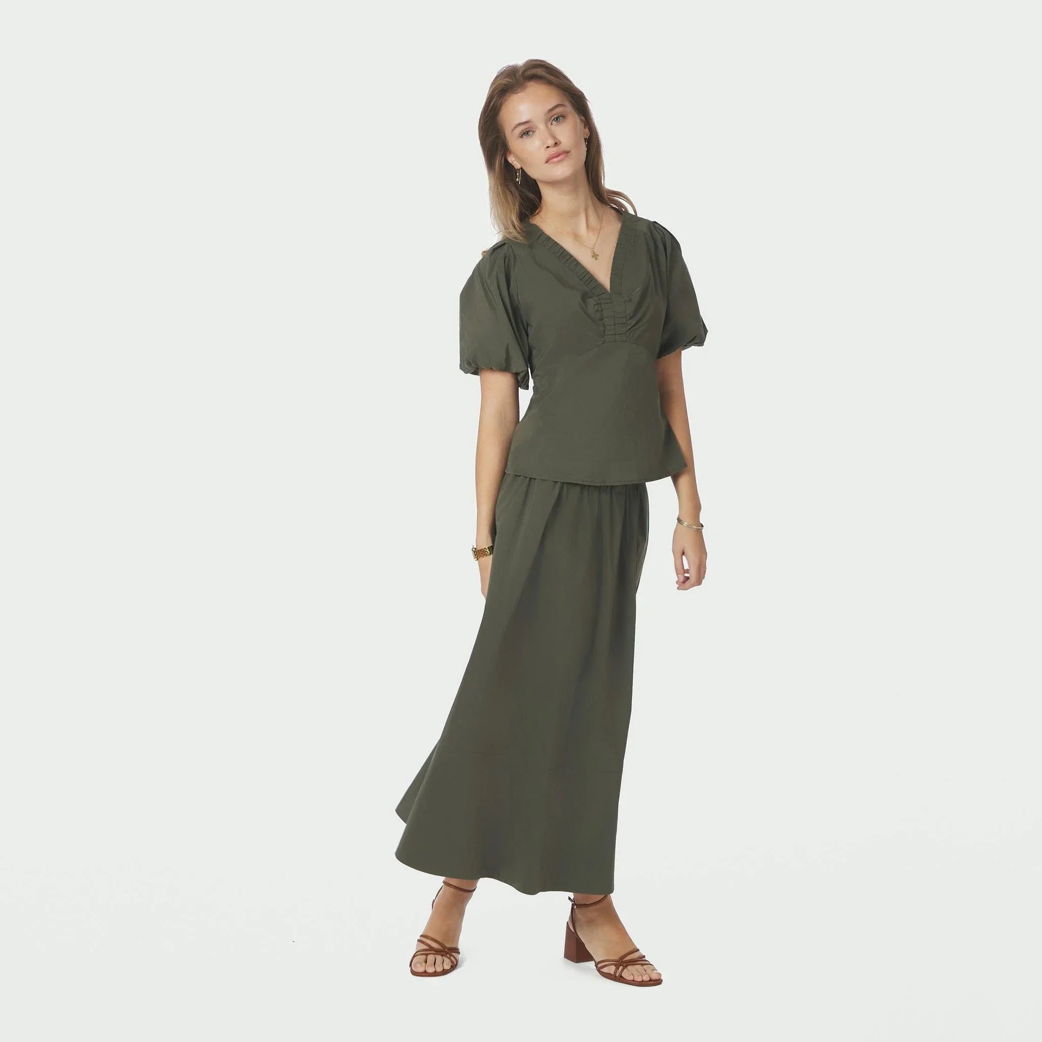 Model i hel figur i grøn bluse med V-hals stylet med lang grøn nederdel og sandaler