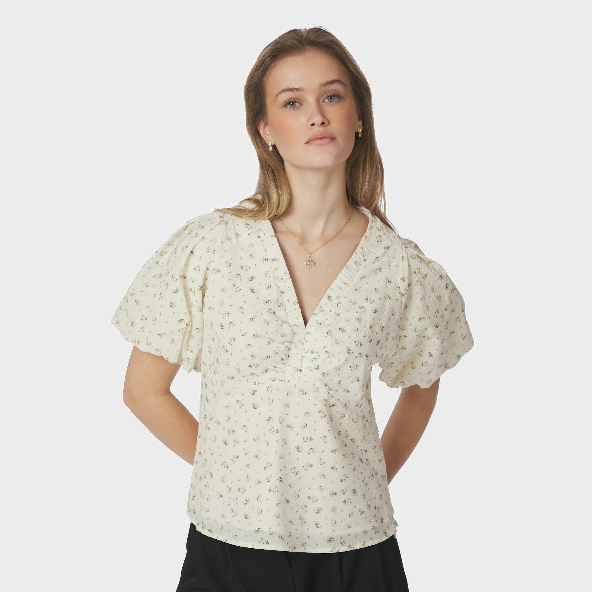 Model i lysegul bluse med blomsterprint og V-udskæring med crepe-detaljer, set forfra