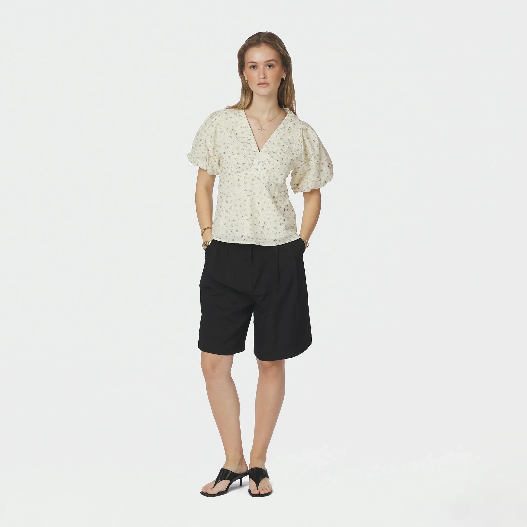 Model i fuld figur i lysegul blomstret bluse stylet med sorte shorts og sandaler