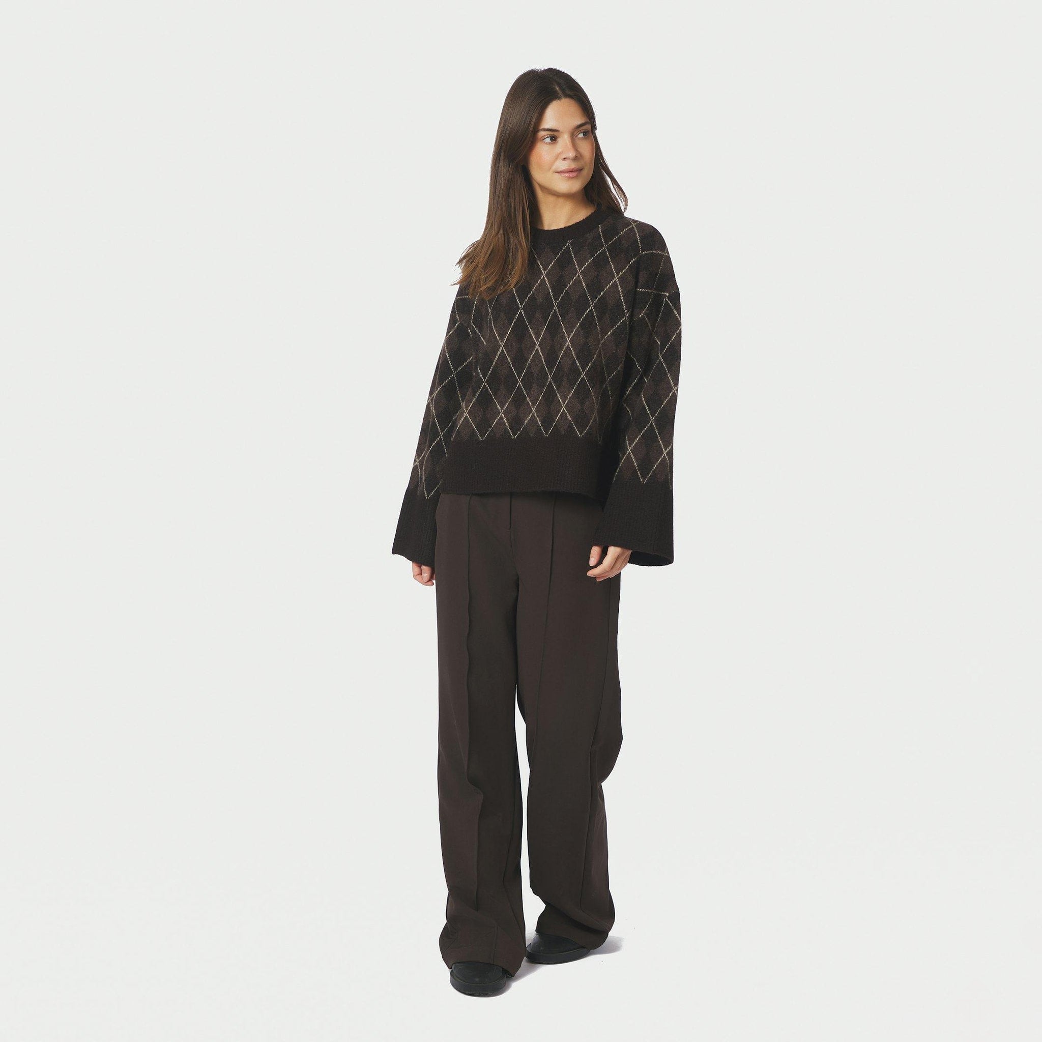 Model i brun argyle strikbluse stylet med brune bukser, fuld figur forfra