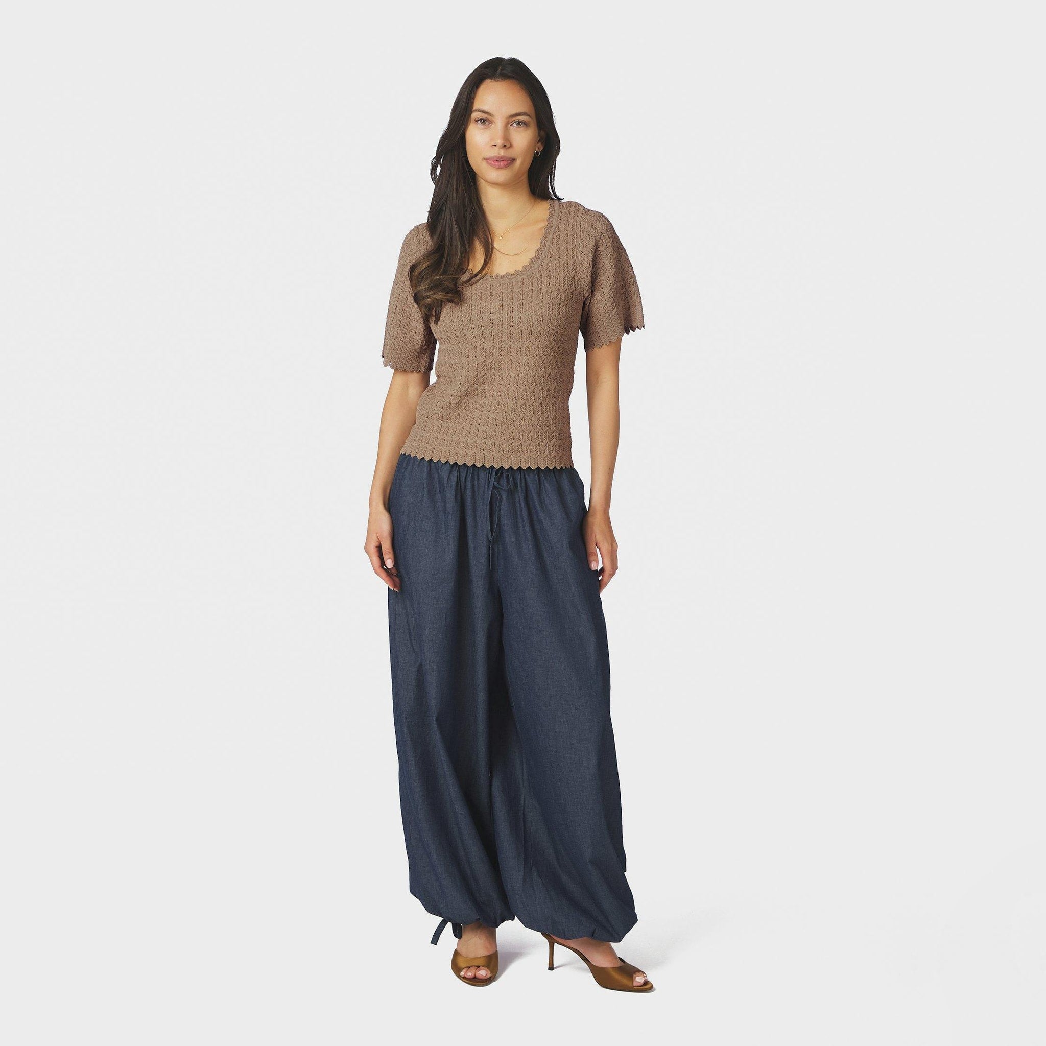 Model i fuld figur i beige hæklet bluse fra Neo Noir stylet med vide bukser i denim