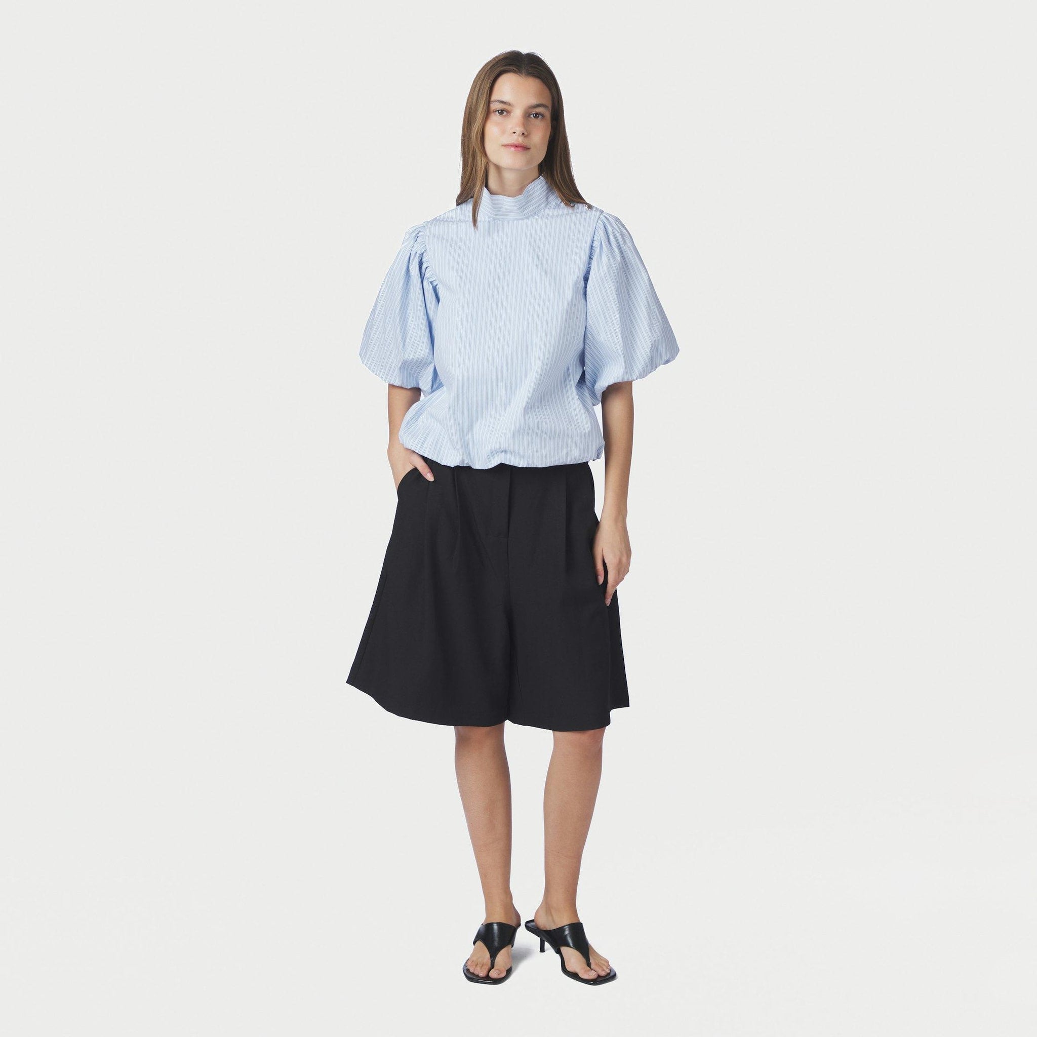 Model i blå stribet bluse med pufærmer stylet med sorte shorts og sorte sandaler med hæl
