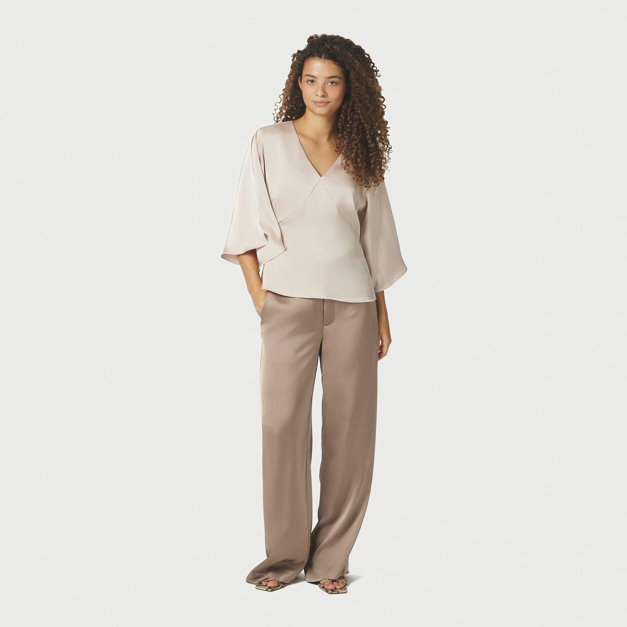 Model i hel figur i beige bluse med V-udskæring stylet med brune vide bukser