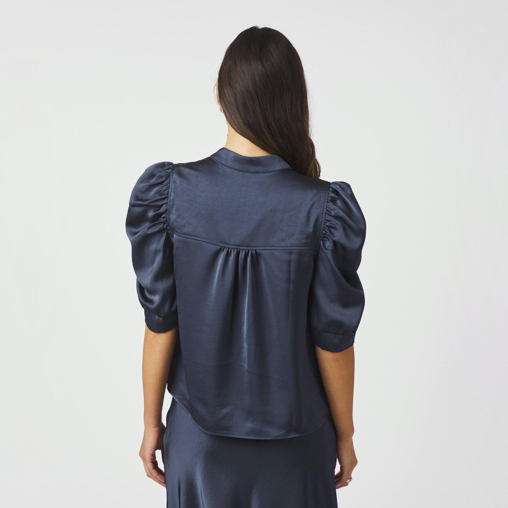 Model set bagfra i navy satinbluse med puffede ærmer og bærestykke