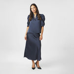 Model i navy satinbluse stylet med lang nederdel og sorte pumps, helfigur