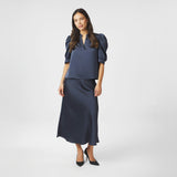 Model i navy satinbluse stylet med lang nederdel og sorte pumps, helfigur