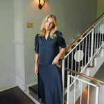 Blond model ved en trappe i navy satinbluse stylet med lang nederdel