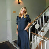 Blond model ved en trappe i navy satinbluse stylet med lang nederdel