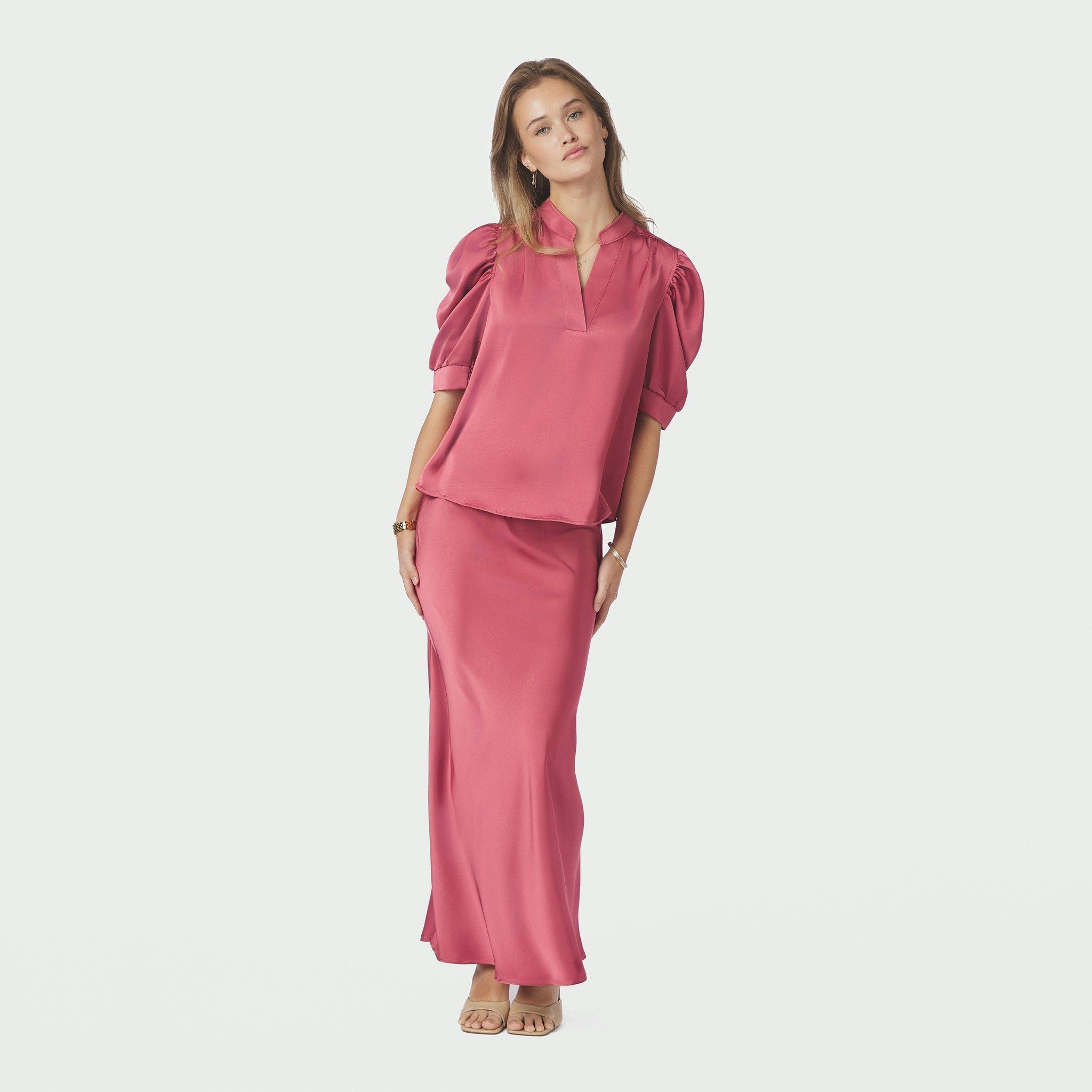Model i hel figur i pink satinbluse Roella stylet med lang satinnederdel i samme farve