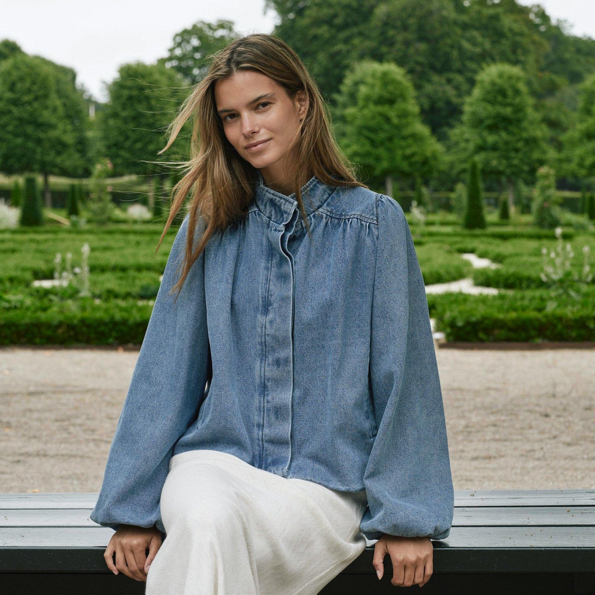 Model siddende udendørs i blå denimjakke med brede ærmer