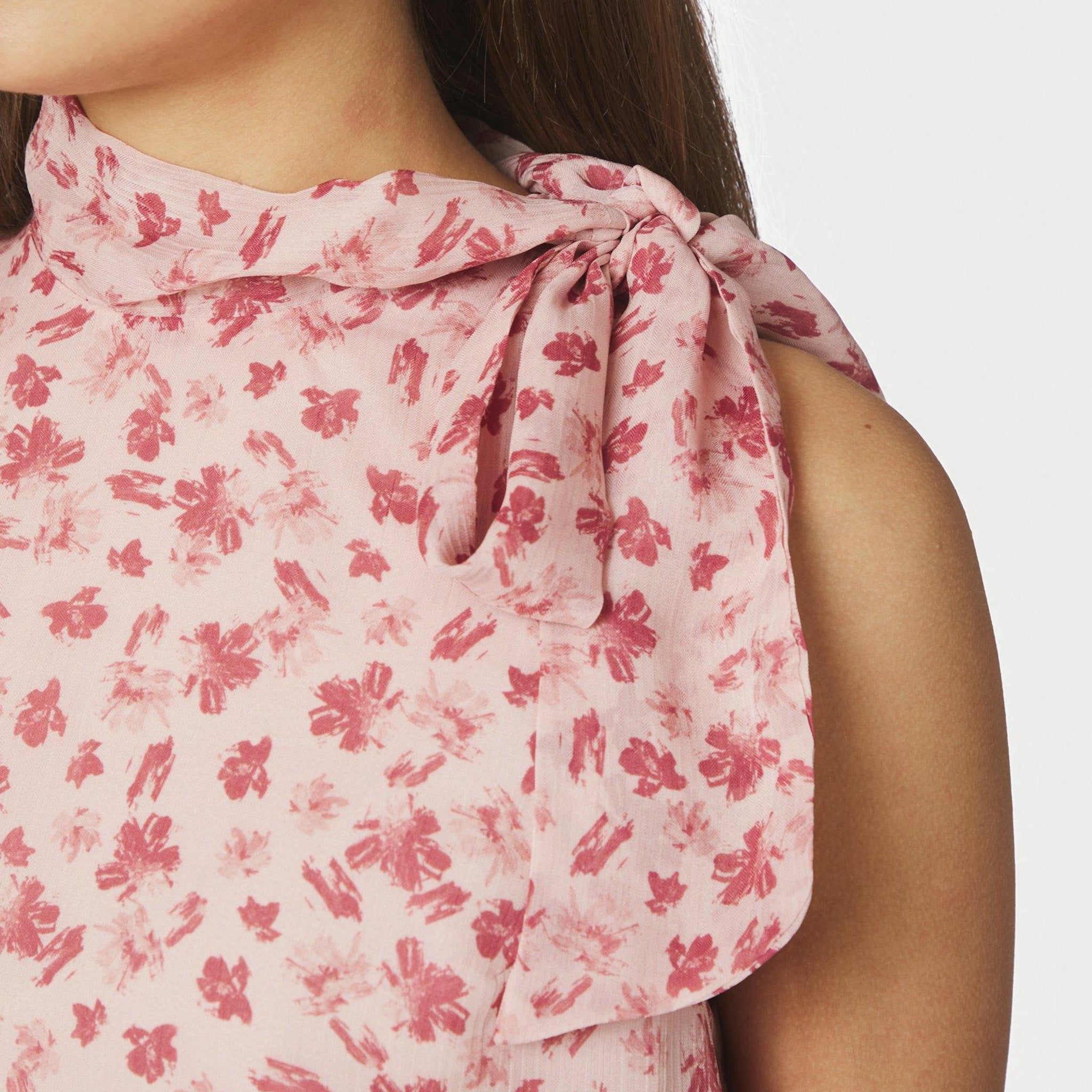 Nærbillede af sløjfebånd ved halsen på pink top med blomsterprint