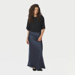 Model i hel figur med lang navy nederdel i satin, sort t-shirt og ballerinaer