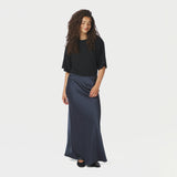 Model i hel figur med lang navy nederdel i satin, sort t-shirt og ballerinaer