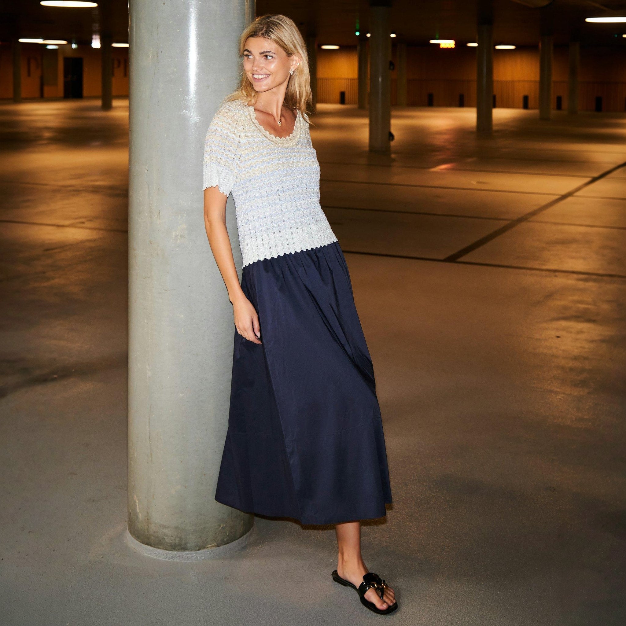 Model i navy maxinederdel stylet med lys strikbluse og sorte sandaler