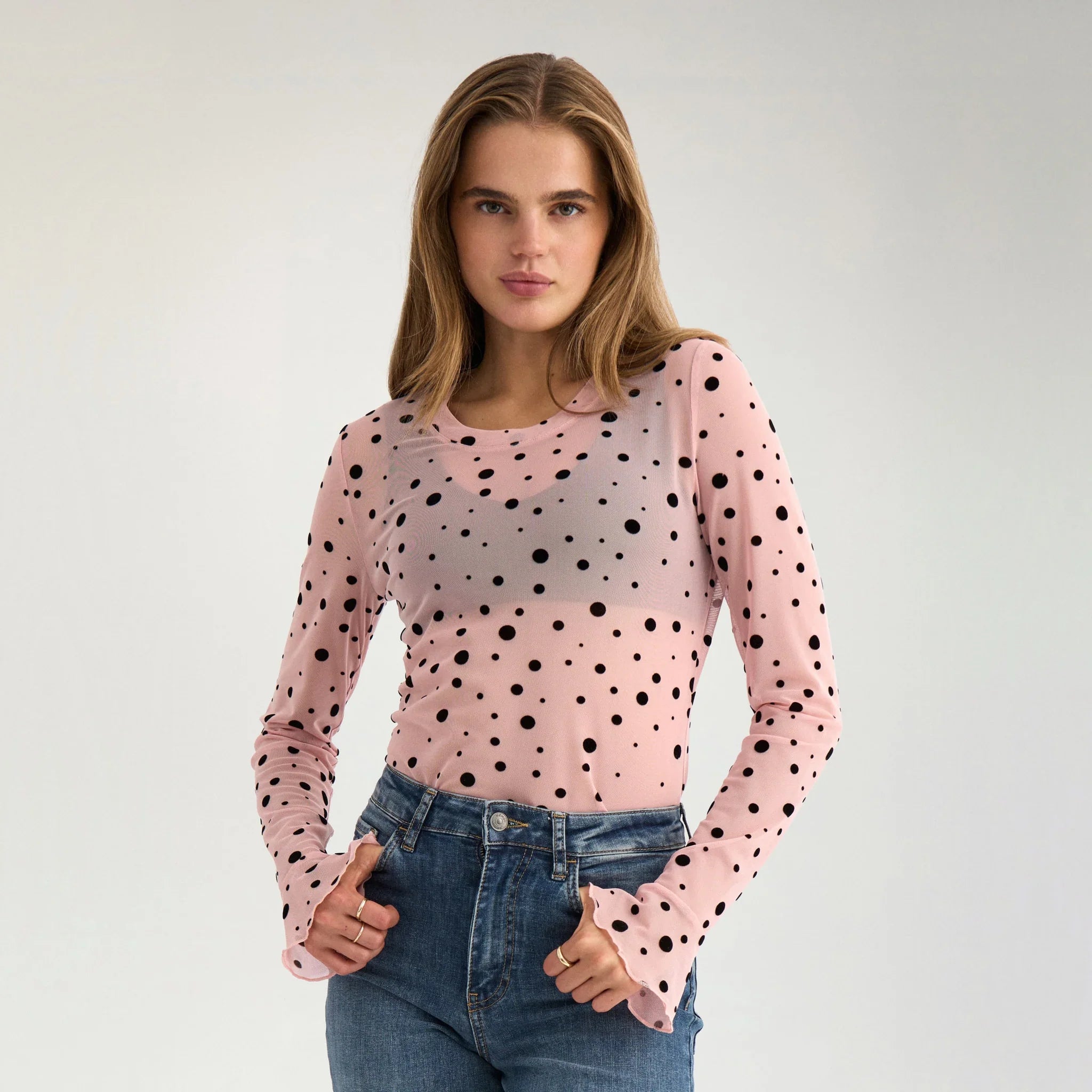 Model i gennemsigtig orange mesh t-shirt med sorte prikker og jeans, tæt på forfra