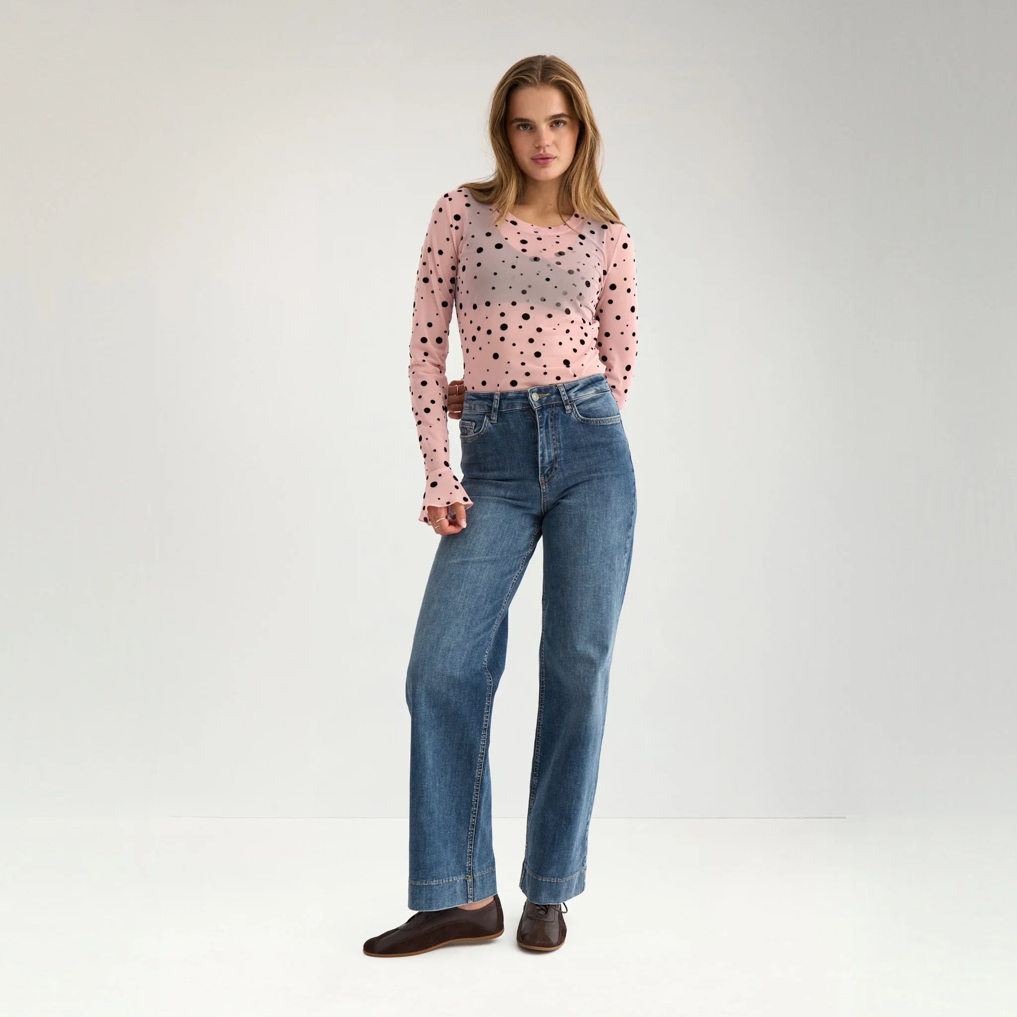 Model i hel figur i langærmet prikket mesh t-shirt i farven Peachskin med blå jeans