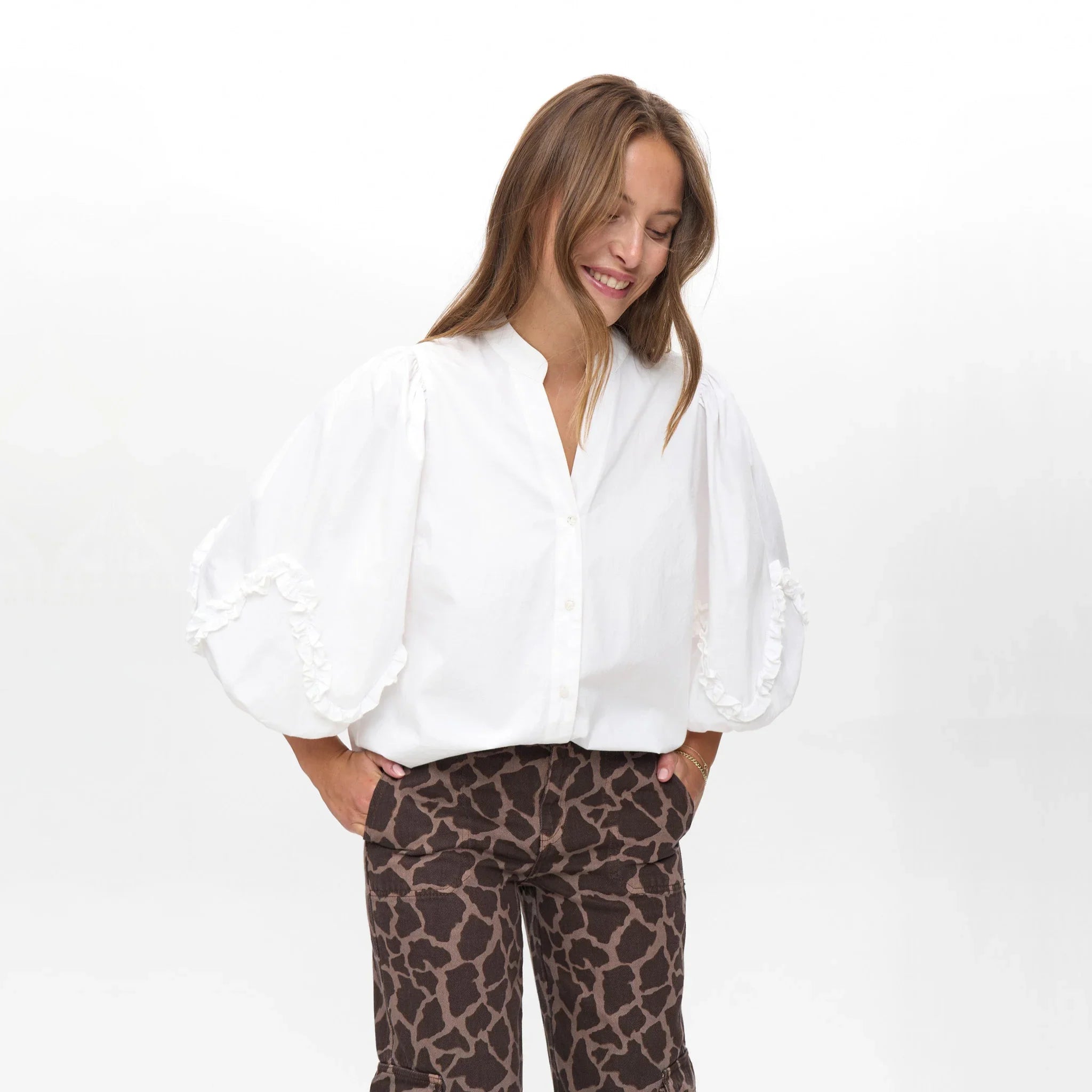 Smilende model i hvid bluse med store puffede ærmer og flæser