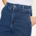 Nærbillede af blå jeans med knap foran, bæltestropper og skrå sidelomme