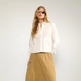 Model i hele figuren i kort hvid skjorte med lange ærmer, stylet med beige midi-nederdel