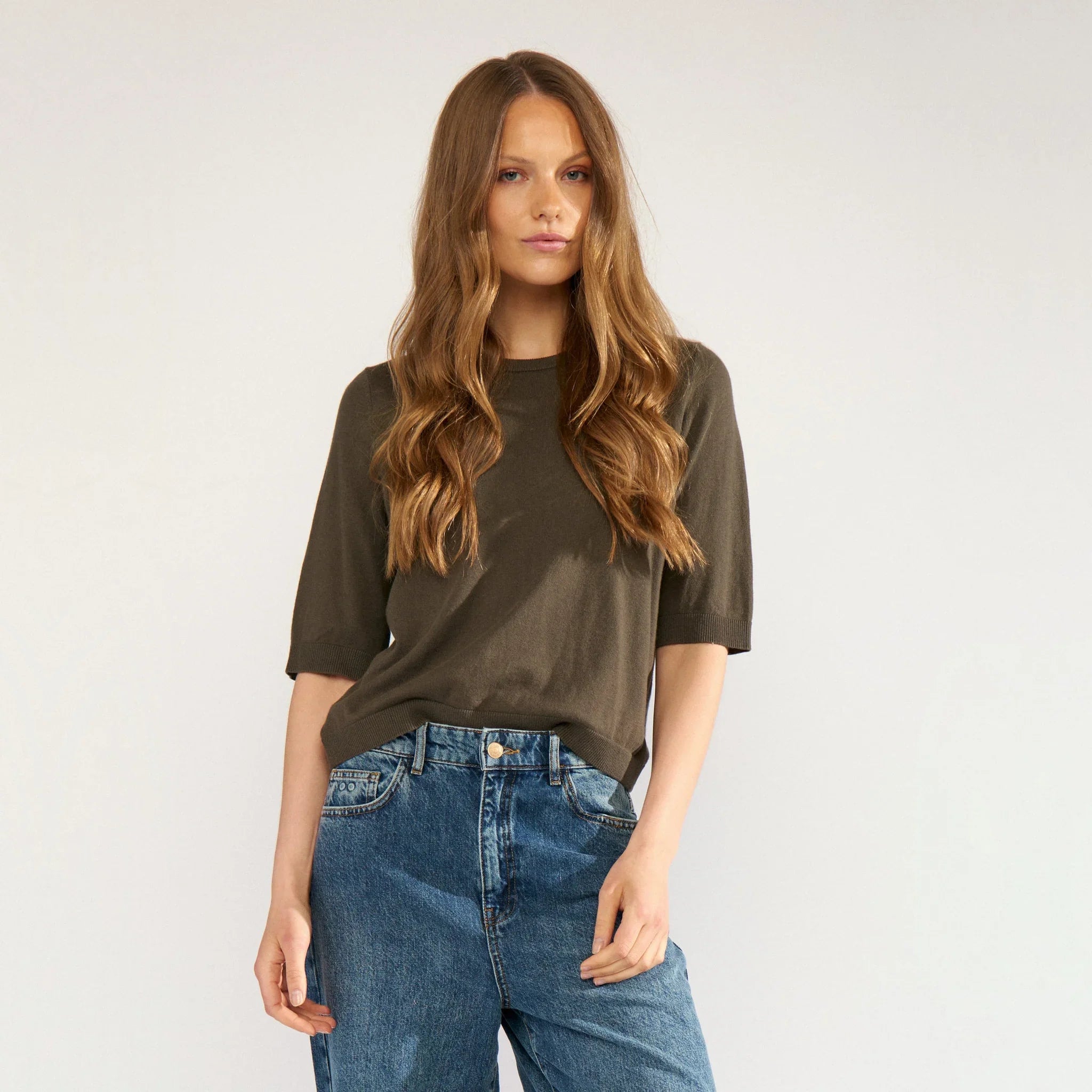 Model i kortærmet grøn pullover fra Nümph sammen med blå jeans, set tæt på forfra