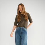 Model i fuld figur i grøn Nucally pullover stylet med vide blå jeans og sorte loafers